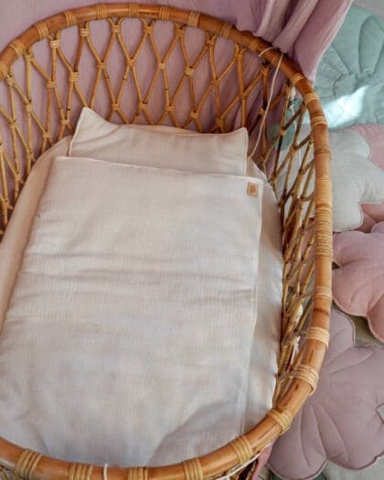 Bambusowy kosz niemowlęcy z białą pościelą obok kolorowych, kwiatowych mat w pastelowych kolorach