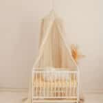 Biała łóżeczko dziecięce z zasłoną w jasnym pokoju o minimalistycznym wystroju i neutralnych kolorach