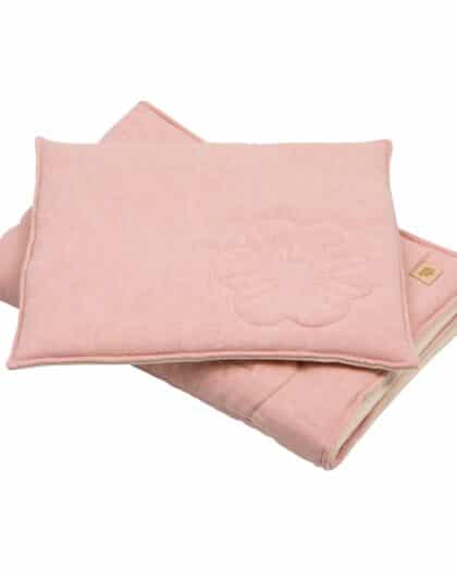 Różowy miękki kocyk z poduszką ozdobioną delikatnym kwiatowym wzorem, złożone na białym tle