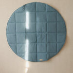 Okrągła, pikowana mata w kolorze niebieskim na beżowym tle z refleksami światła słonecznego