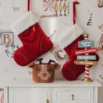 Dwa czerwone świąteczne skarpety z białym futrzanym obszyciem wiszą na ścianie nad komódką z ozdobami świątecznymi