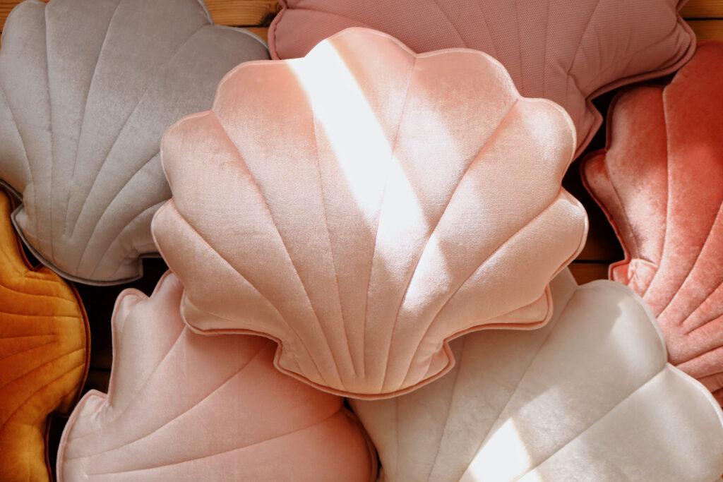 Poduszki w kształcie muszli w pastelowych odcieniach różu, beżu i pomarańczu ułożone jedna na drugiej