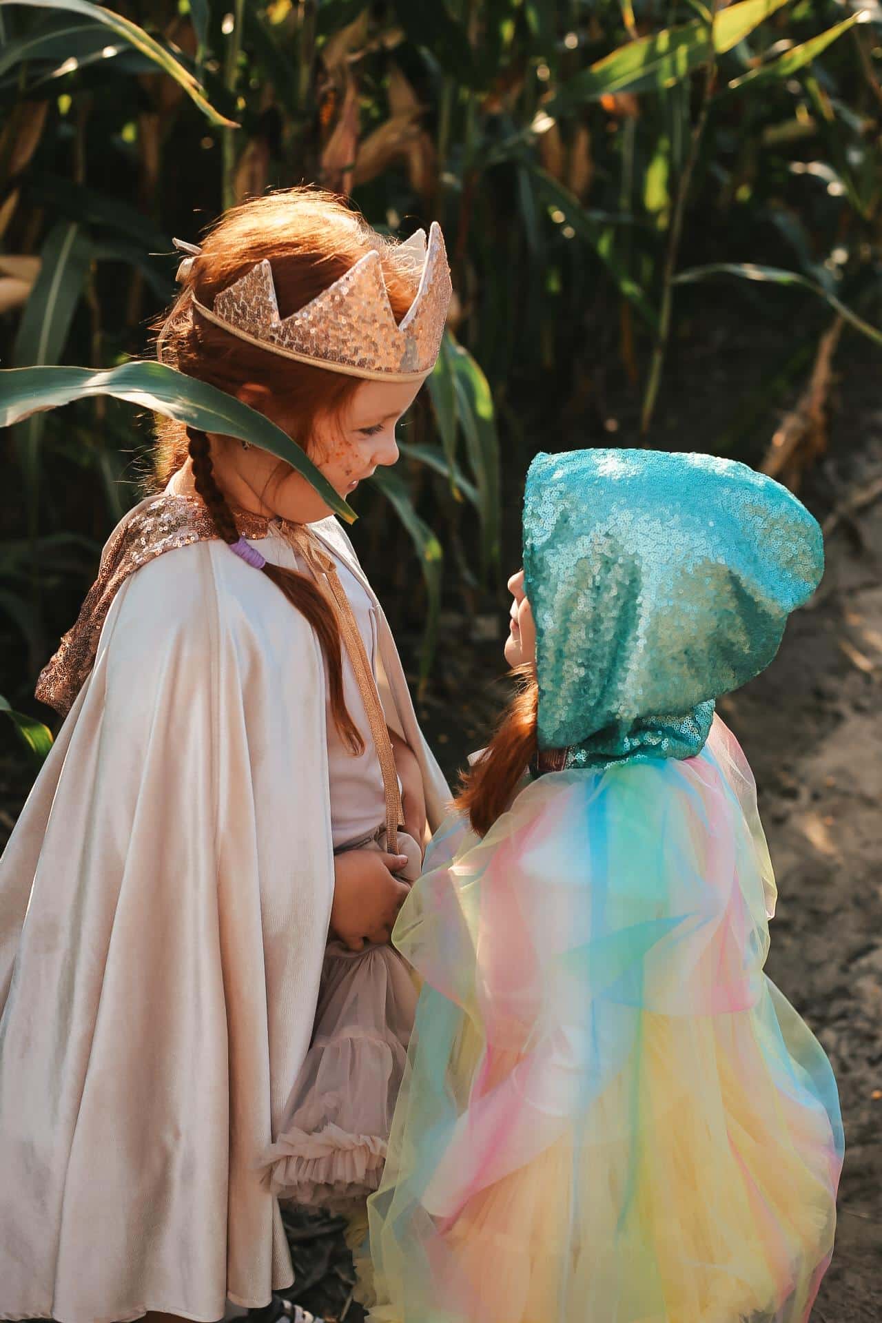 Dwie dziewczynki w kolorowych kostiumach bawiące się na tle zielonej roślinności w słoneczny dzień