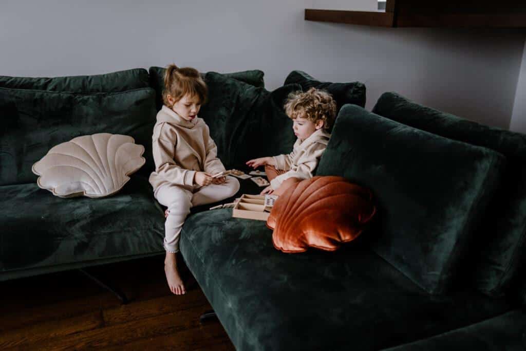 Dwoje dzieci siedzi na ciemnozielonej kanapie i bawi się drewnianymi zabawkami w przytulnym salonie