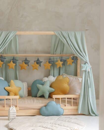 Dziecięce łóżko drewniane z miękkimi poduszkami w kształcie gwiazd i obłoków oraz pastelowymi zasłonami