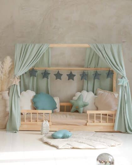 Drewniane łóżko dziecięce z zielonymi zasłonami i miękkimi poduszkami w kształcie gwiazd i muszelek