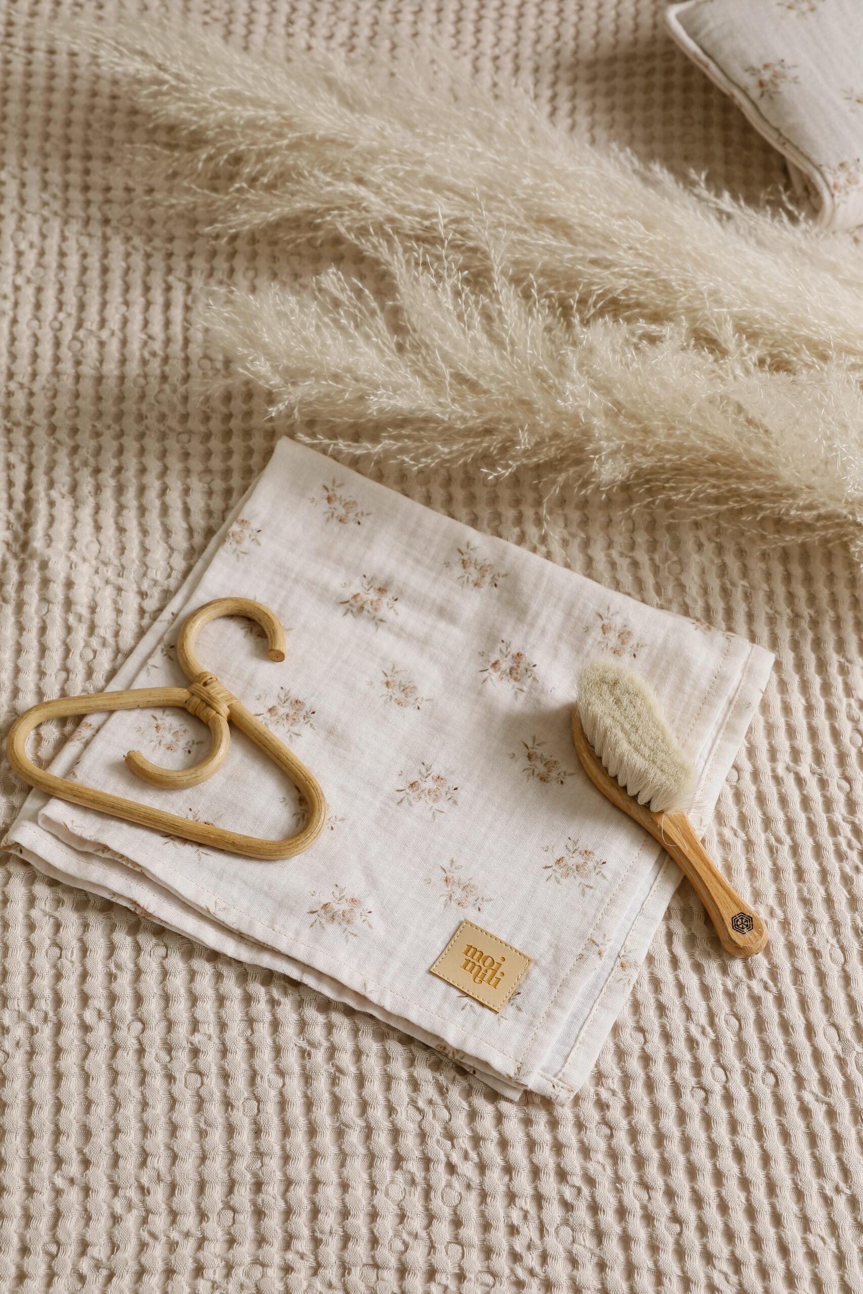 Naturalne materiały do pielęgnacji niemowląt na beżowym tle, z szczotką, wieszakiem i ściereczką z kwiatowym wzorem