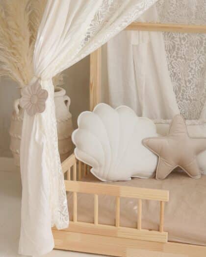 Drewniane łóżeczko dziecięce z białą koronkową zasłoną i poduszkami w kształcie muszli i gwiazdy
