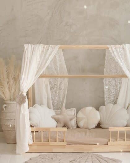 Drewniane łóżko dziecięce z beżowymi i białymi poduszkami w kształcie muszli i gwiazdy oraz zasłonami