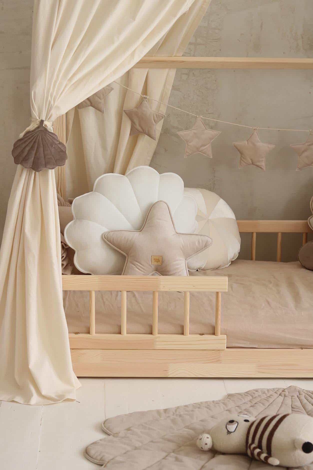 Drewniane łóżeczko dziecięce z kremowymi poduszkami w kształcie gwiazdy i muszli oraz zasłoną