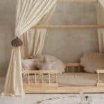 Dziecięce łóżko z drewnianą ramą, kremowymi zasłonami i ozdobnymi poduszkami w kształcie muszelek