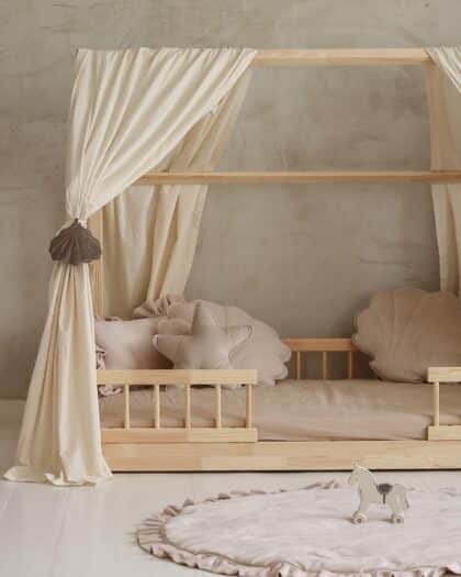 Dziecięce łóżko z drewnianą ramą, kremowymi zasłonami i ozdobnymi poduszkami w kształcie muszelek