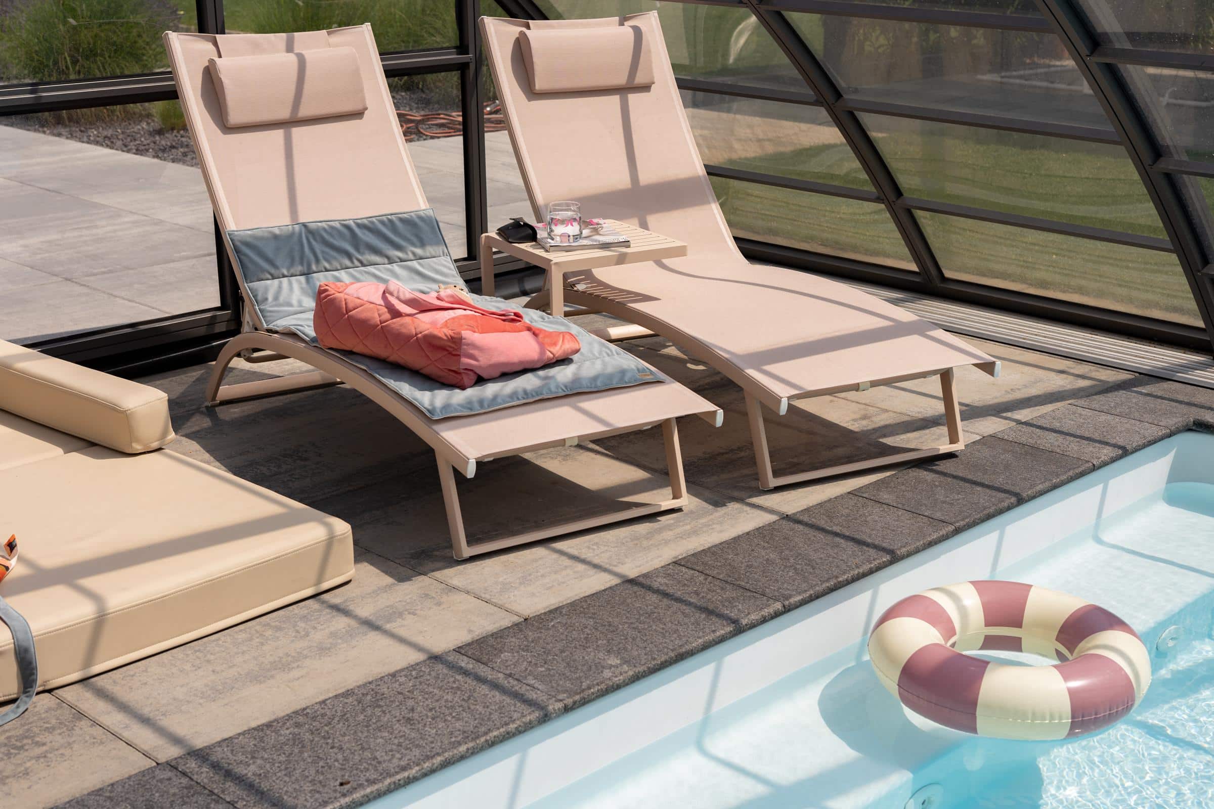 Leżaki przy basenie w osłoniętej przestrzeni z materacem i dmuchanym kołem ratunkowym na wodzie