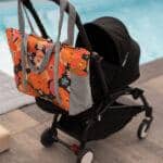 Wielokolorowa torba z kwiatowym wzorem zawieszona na czarnej rączce wózka dziecięcego obok basenu.