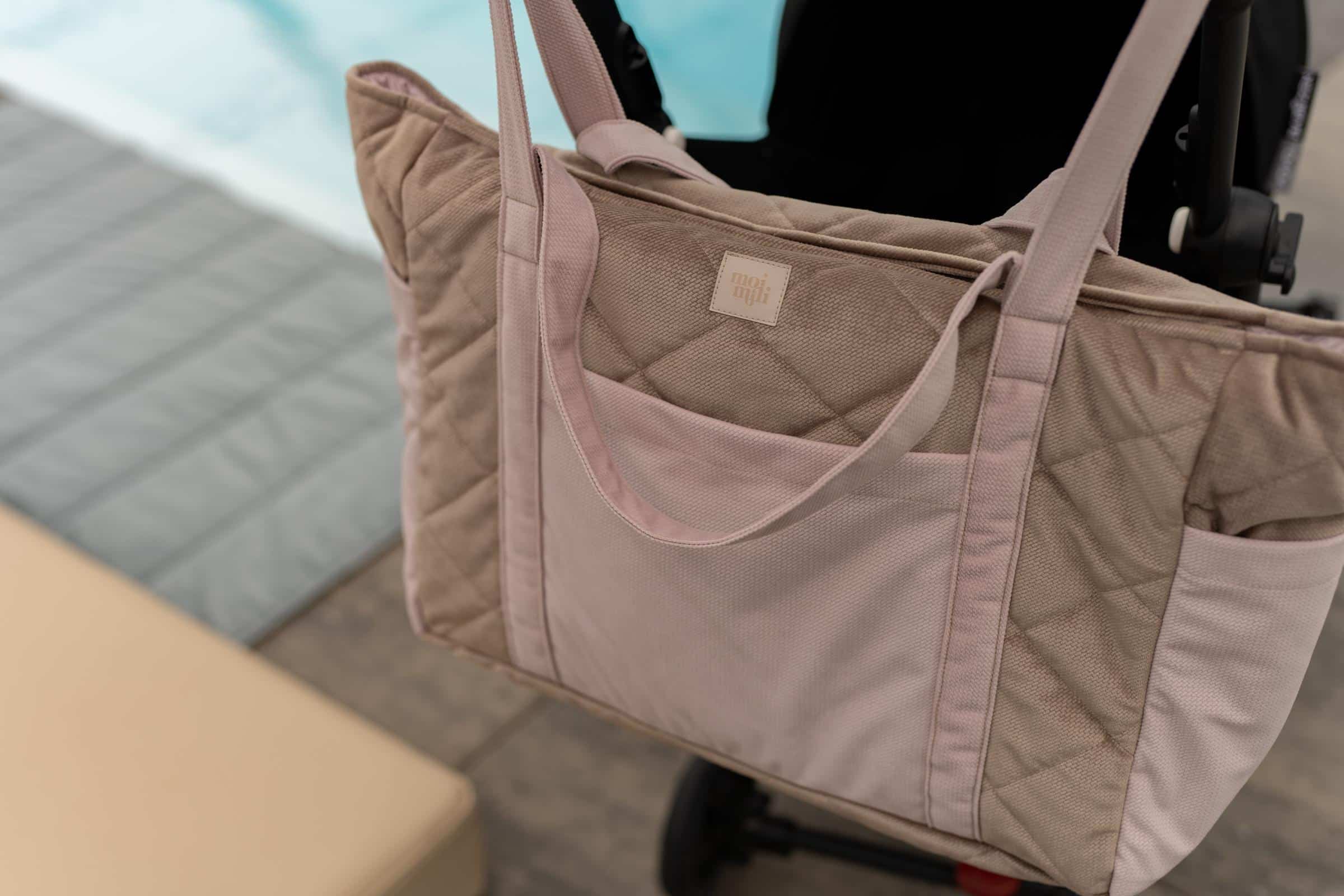 Beżowa pikowana torba z długimi uchwytami zawieszona na rączce czarnego wózka dziecięcego