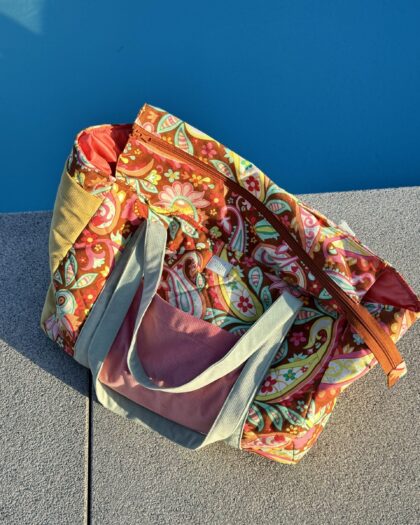 Kolorowa torba plażowa z kwiatowym wzorem leżąca na szarym chodniku obok niebieskiego basenu