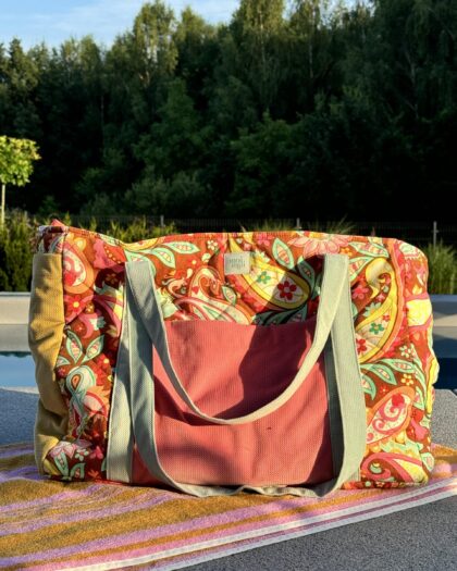 Kolorowa torba plażowa z różowym frontem i wzorem paisley leży na ręczniku obok basenu w słoneczny dzień