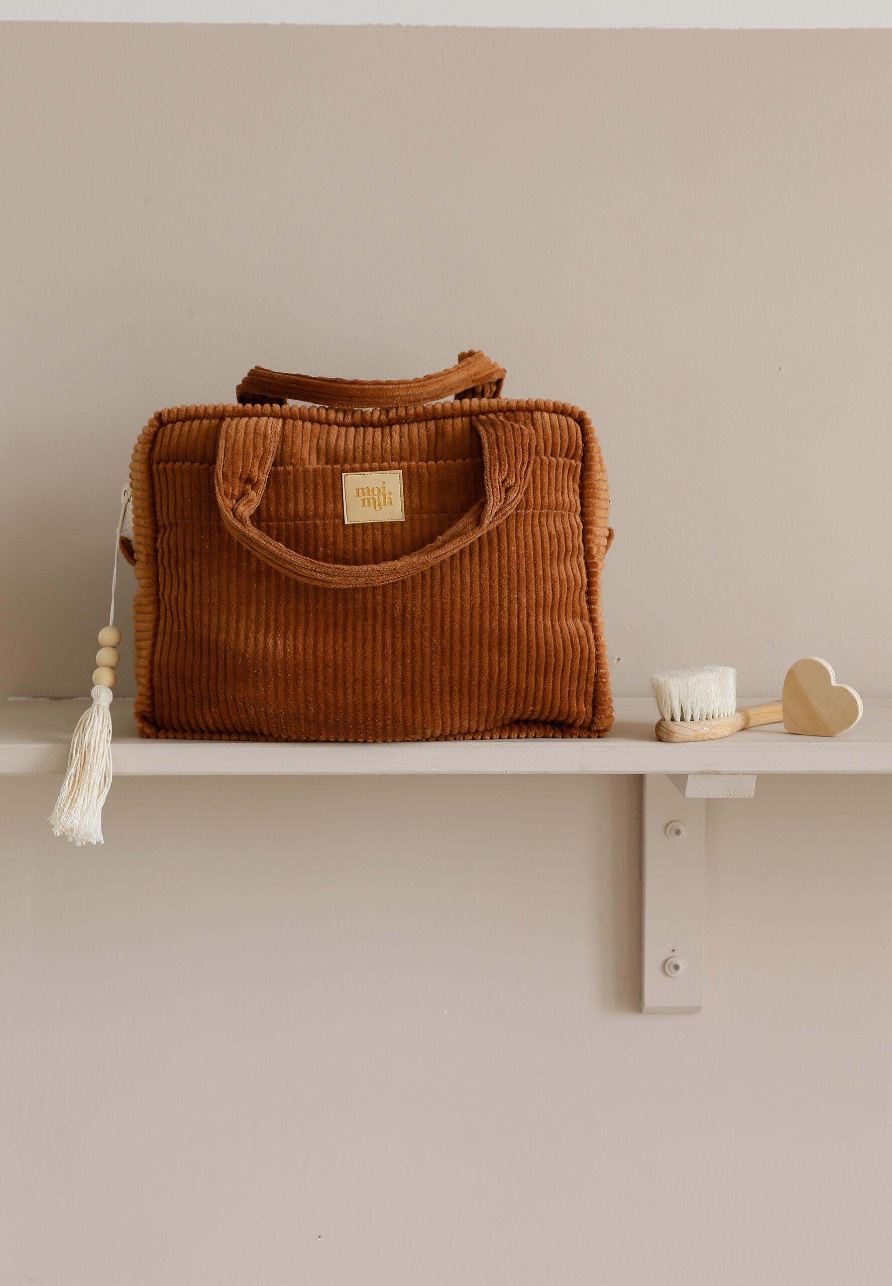 Brązowa torba z materiału sztruksowego na półce obok drewnianego pędzla do włosów o kształcie serca