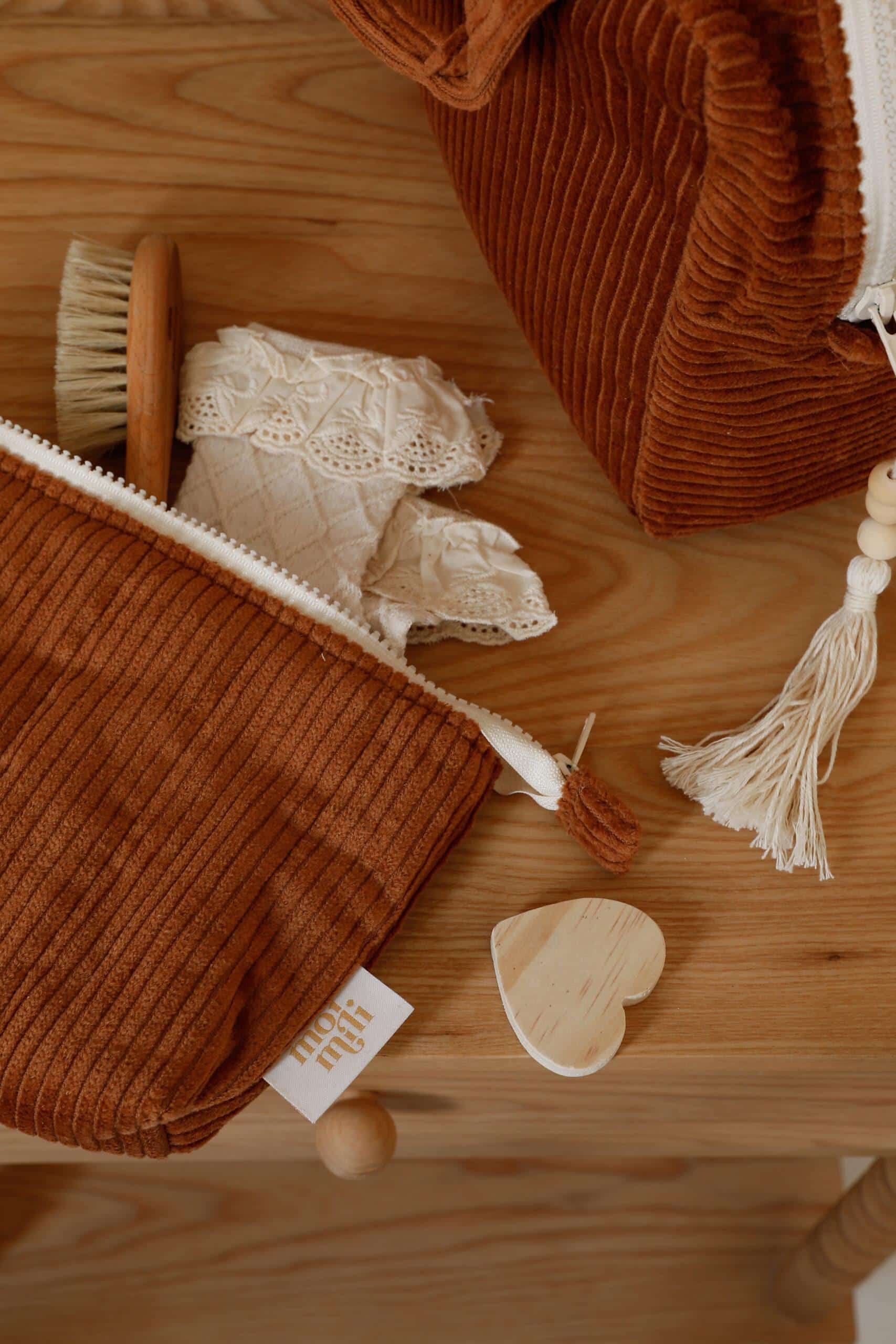 Brązowe kosmetyczki z prążkowanego materiału na drewnianym stole, z koronkową tkaniną i drewnianą szczotką w środku