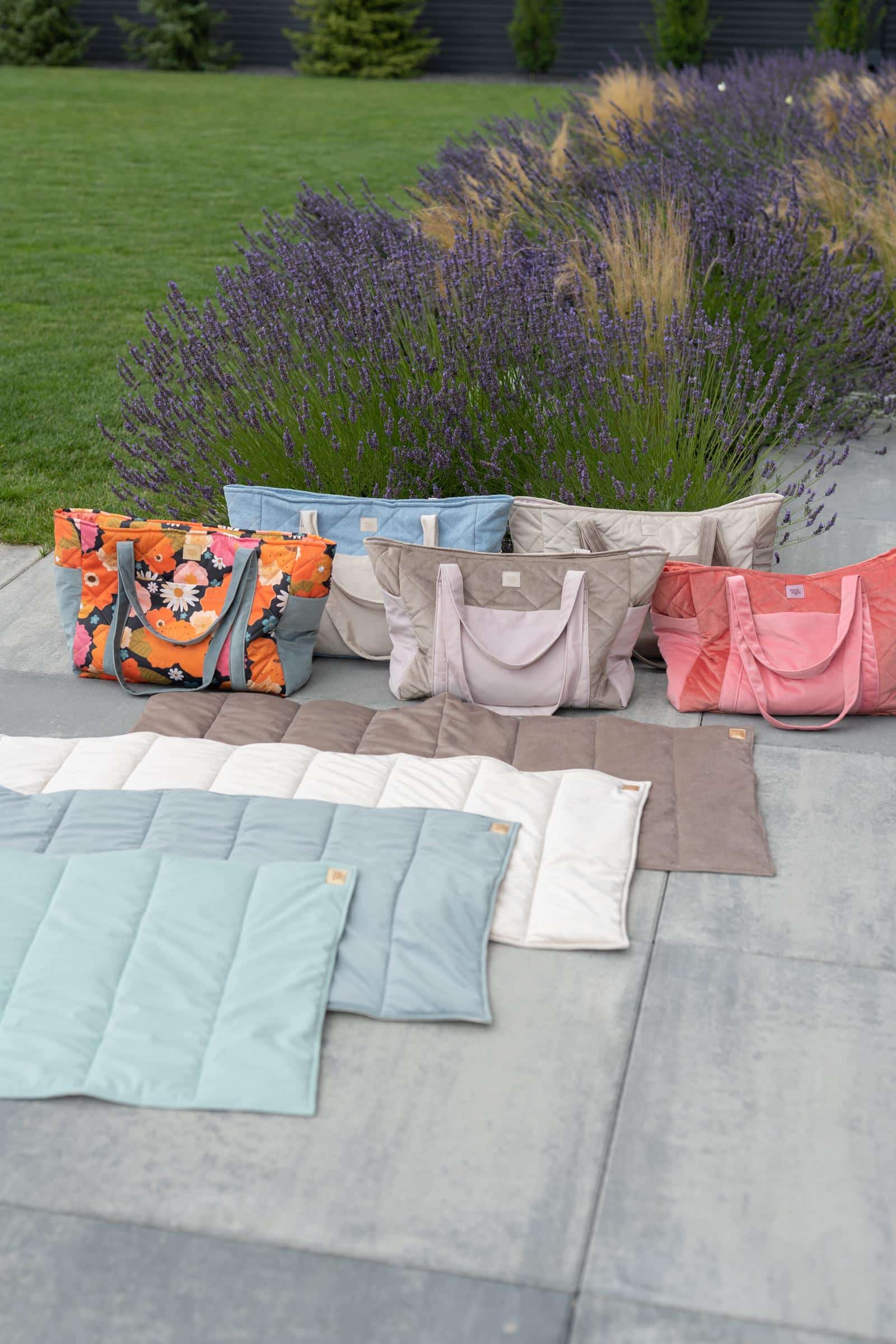 zestaw kolorowych toreb i mata w różnych odcieniach na tle lawendy i trawnika w ogrodzie