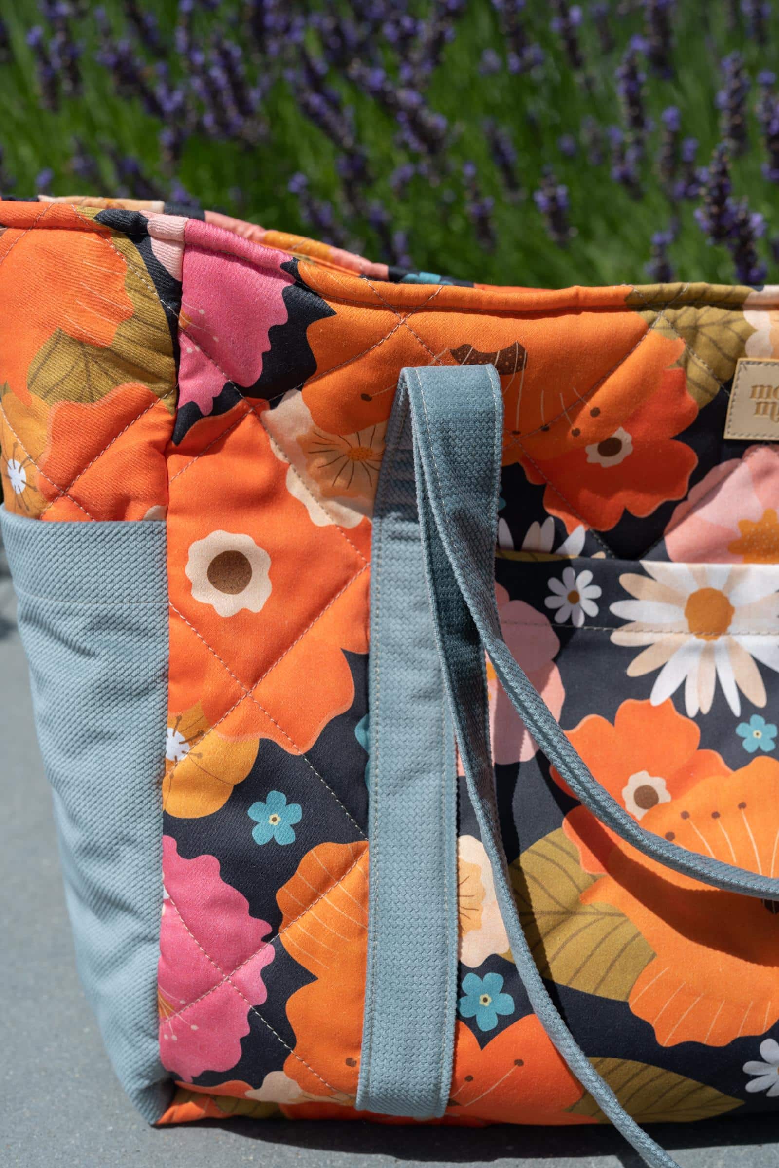 Torba na ramię z materiału w jaskrawe kwiaty w odcieniach pomarańczu i różu na tle zieleni lawendy