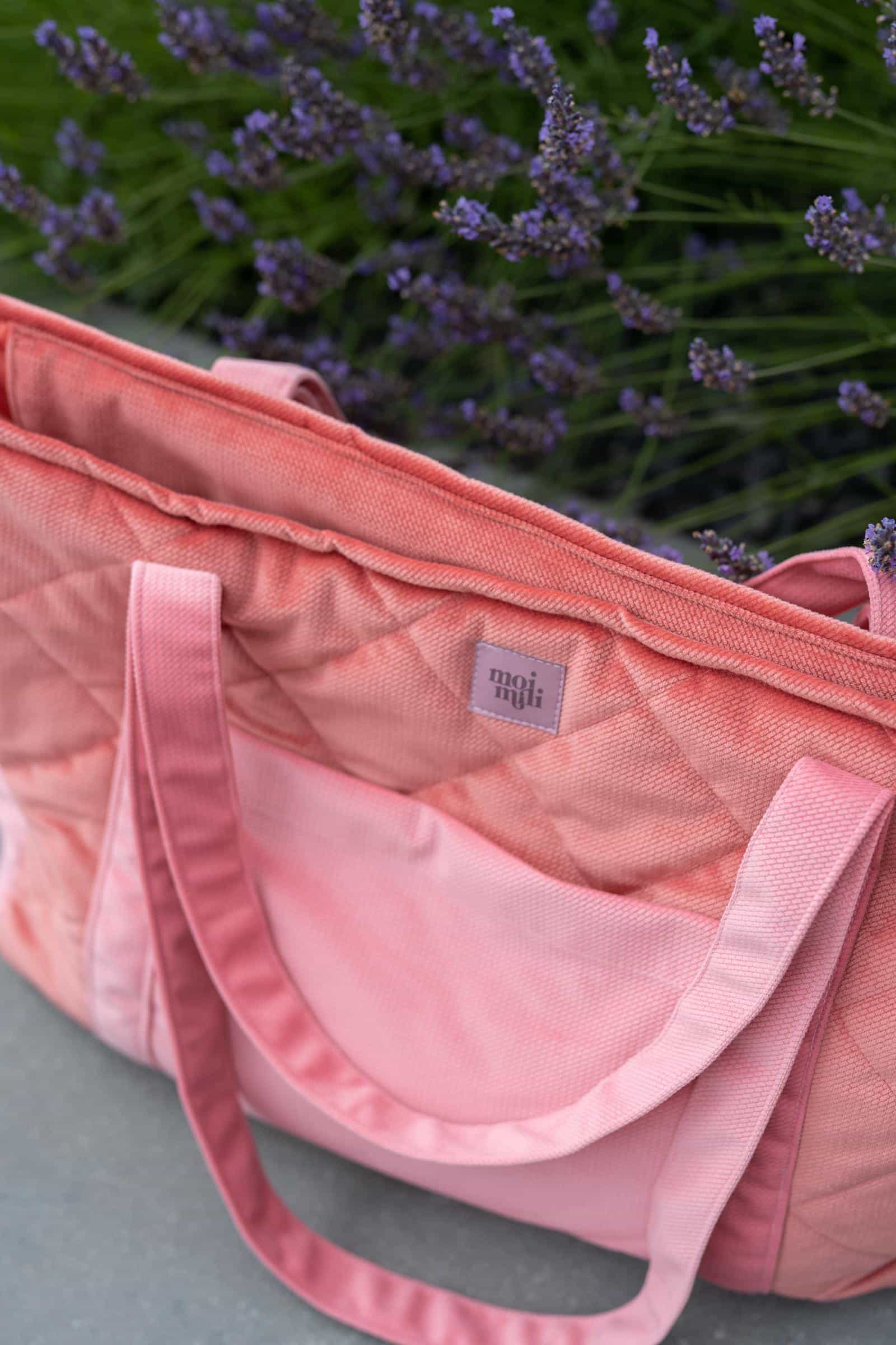 Różowa pikowana torba na ramię z długimi uchwytami na tle kwitnącej lawendy