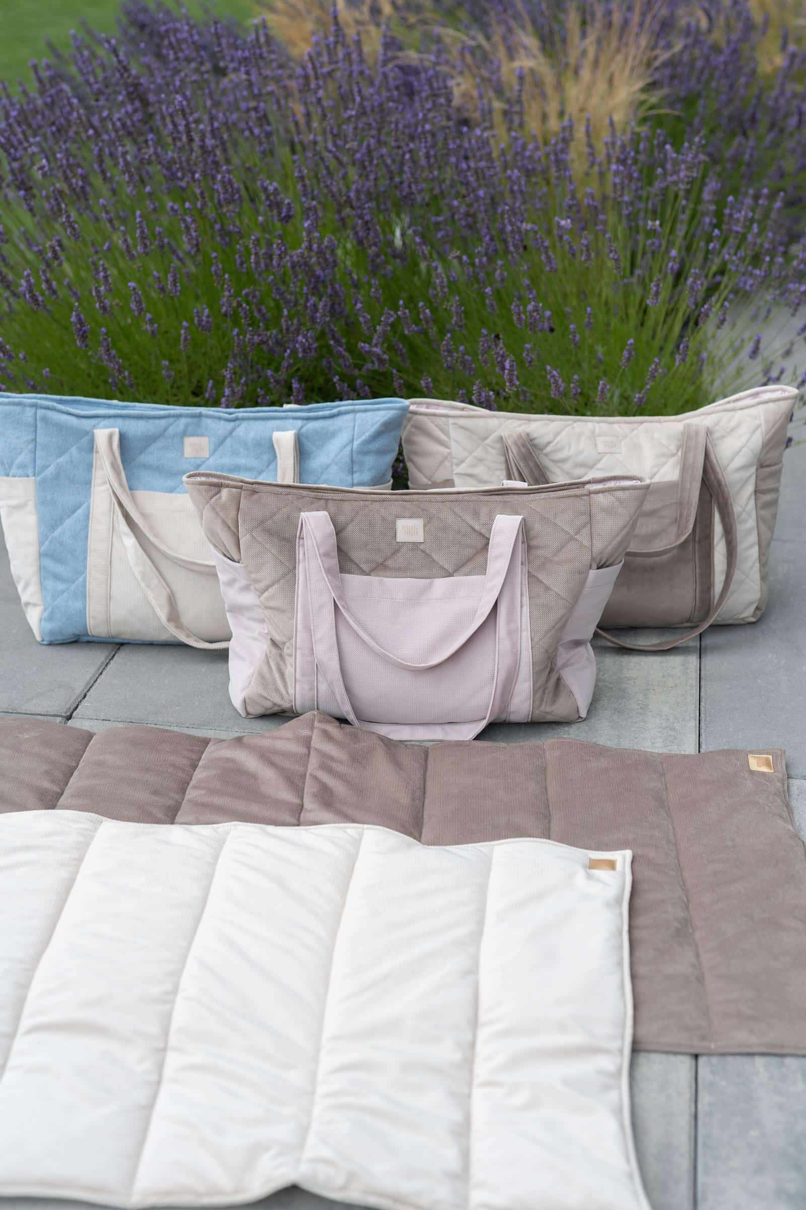 Trzy pikowane torby w odcieniach beżu i niebieskiego na tle lawendy oraz pikowany koc na szarym tle