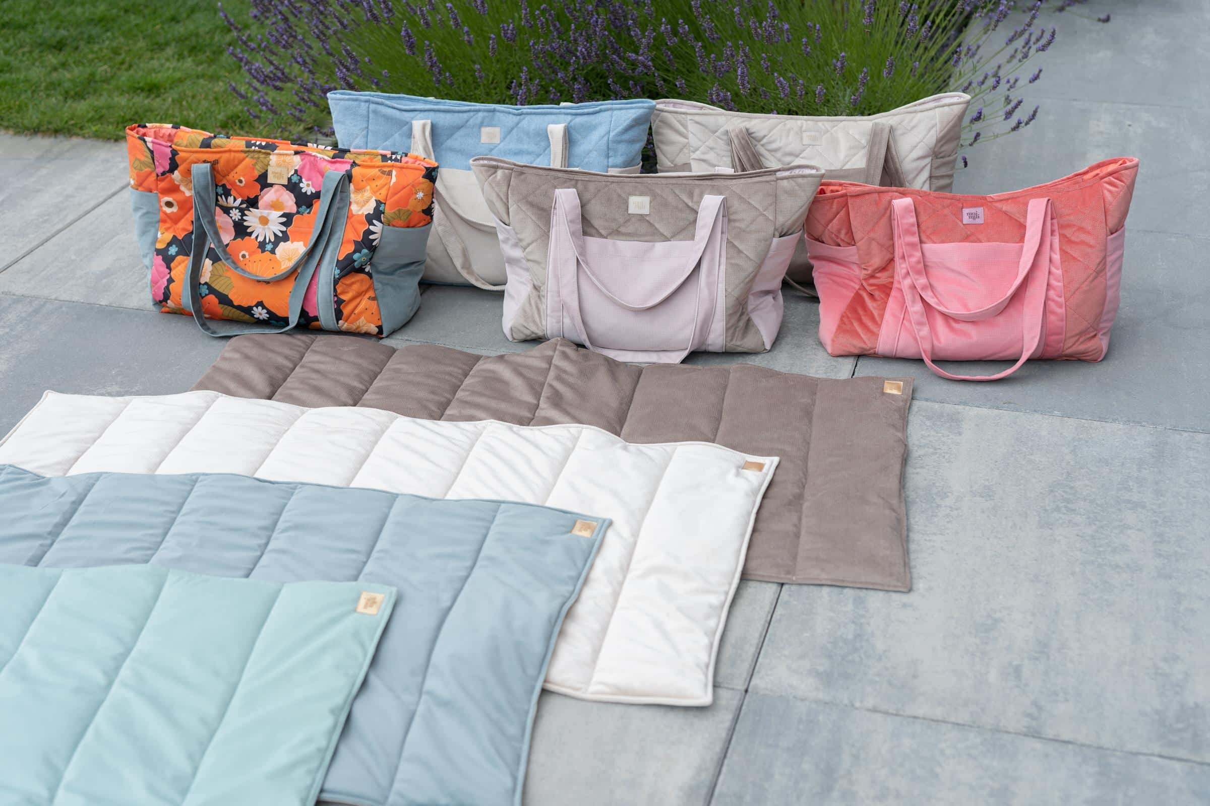 Kolorowe pikowane torby i maty ułożone na tarasie obok zielonego trawnika i lawendy w ogrodzie