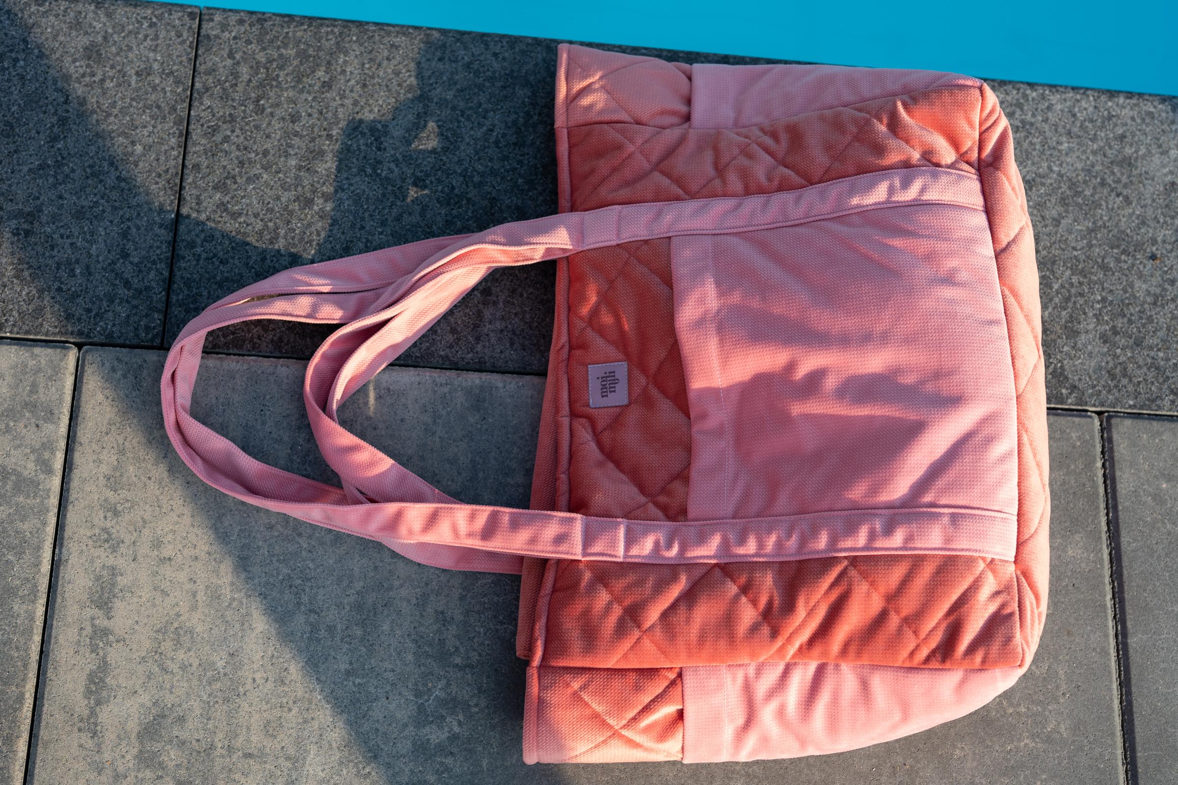 Różowa pikowana torba leżąca na betonowej posadzce przy niebieskiej krawędzi basenu