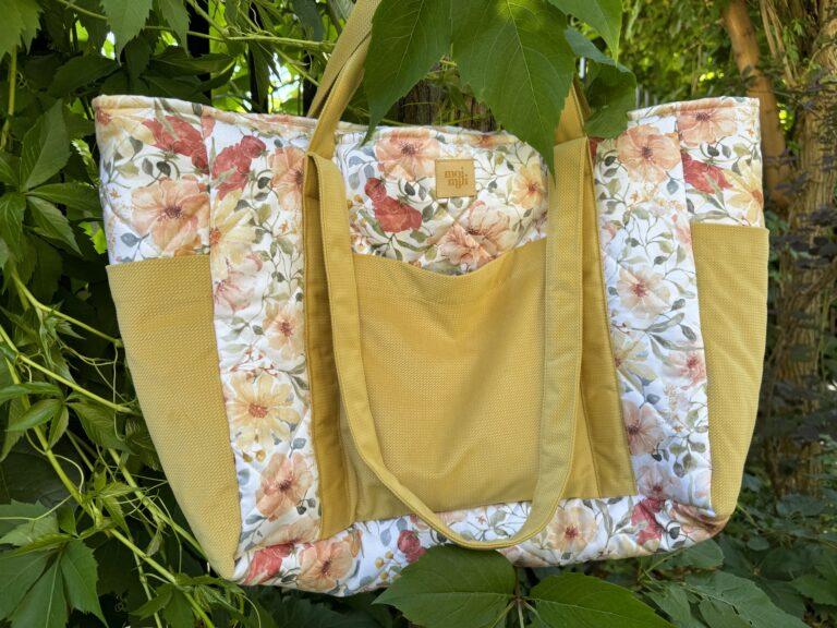 Torba na zakupy z kwiatowym wzorem i żółtymi kieszeniami zawieszona na zielonych liściach