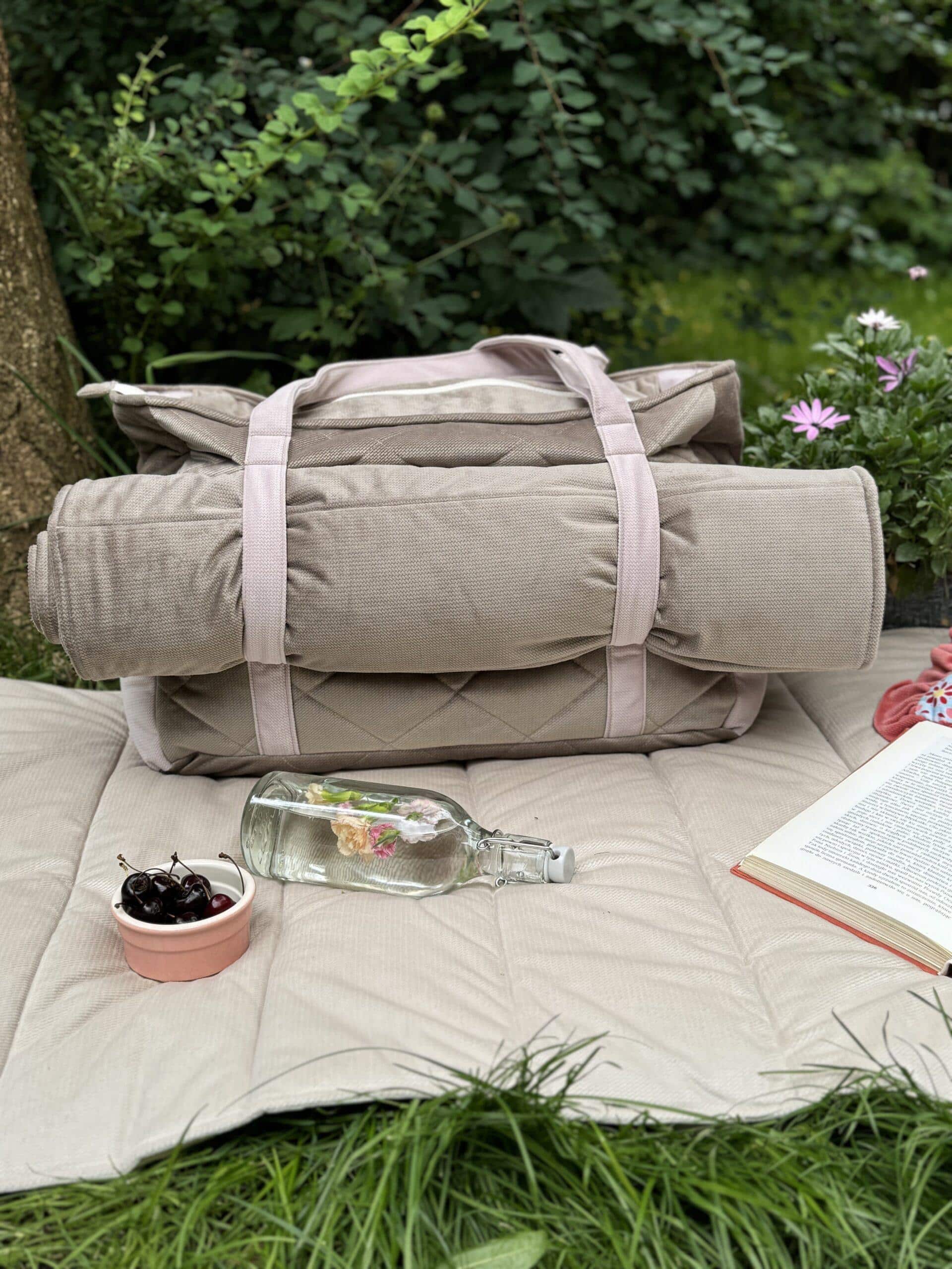 Beżowa składana mata z torbą, butelką wody i miską z czereśniami na trawie w ogrodzie