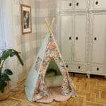 Dziecięcy namiot tipi z kwiatowym wzorem w jasnym pokoju z szafą i obrazem na ścianie.