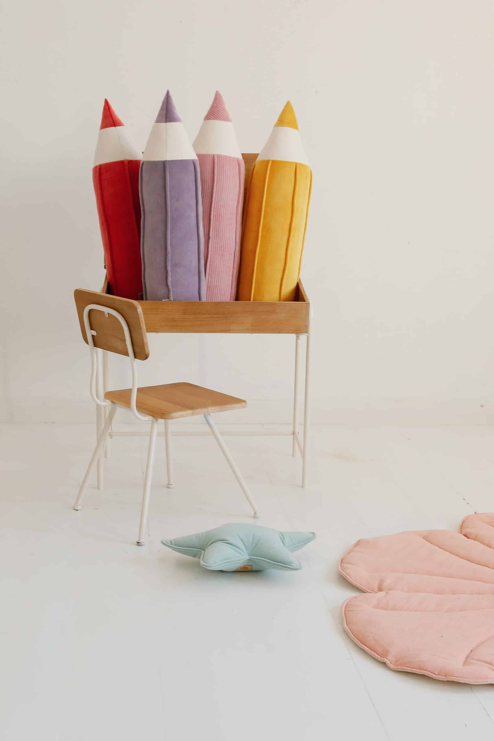 Drewniane biurko z kolorowymi poduszkami w kształcie dużych kredek i niebieską poduszką gwiazdką na podłodze