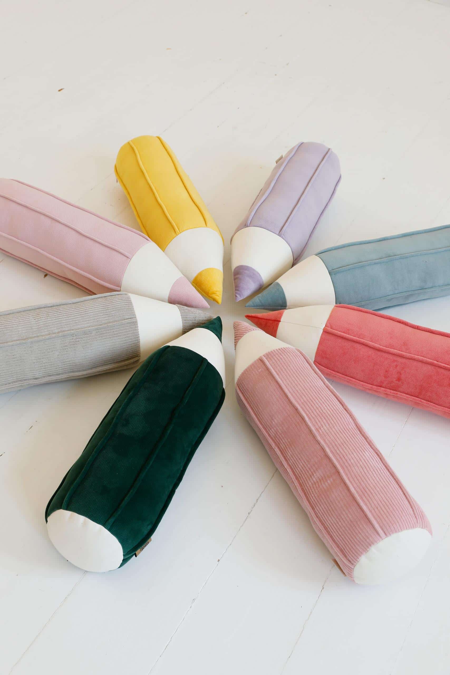 Kolorowe poduszki w kształcie grubych ołówków ułożone w okrąg na białej podłodze