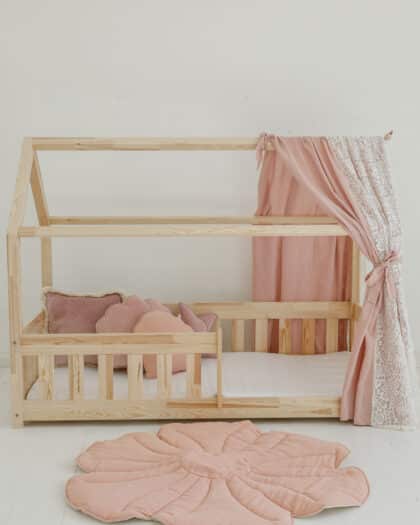 Drewniane łóżko dziecięce w kształcie domku z różowymi zasłonami i kwiatowym miękkim dywanikiem