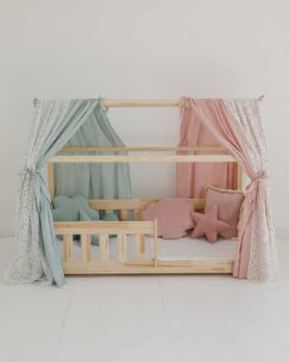Drewniane łóżeczko dziecięce z zasłonami w pastelowych kolorach i poduszkami w kształcie chmury i gwiazdy