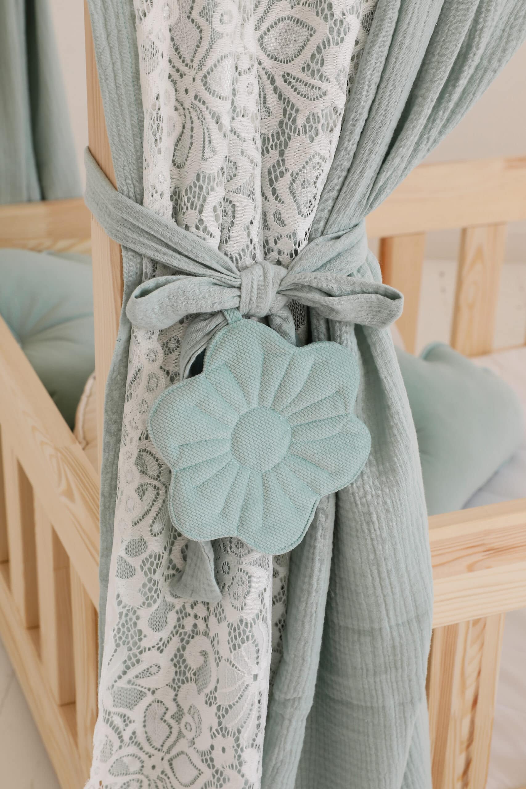Zbliżenie na miękkie miętowe zasłony i białą koronkę z wiązaniem ozdobionym kwiatowym elementem