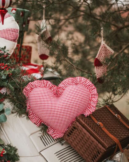 Czerwono-biała sercowata poduszka w kratkę na bagażniku białego auta otoczona świątecznymi dekoracjami