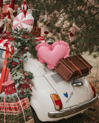 Biały samochód udekorowany świątecznymi girlandami, poduszką w kształcie serca i prezentami na tylnej części