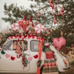 Biały samochód ozdobiony świątecznymi pluszakami, girlandami i prezentami na tle drzewa iglastego