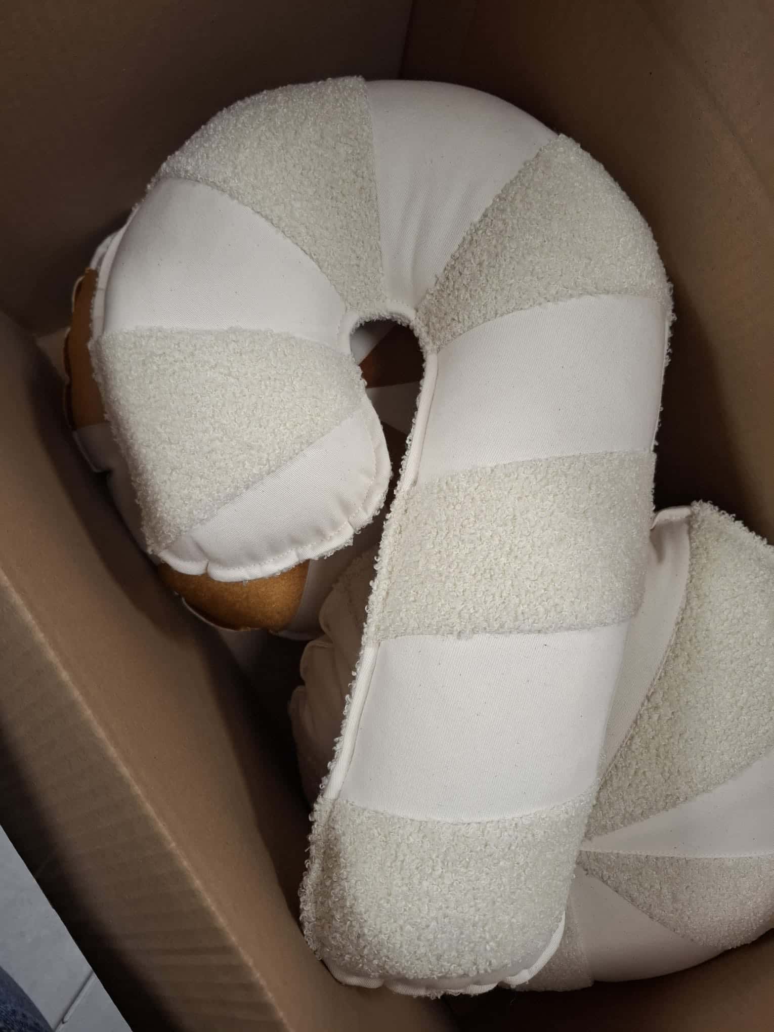 Poduszka podróżna o kształcie podkowy z jasnych materiałów, zapakowana w kartonowe pudełko