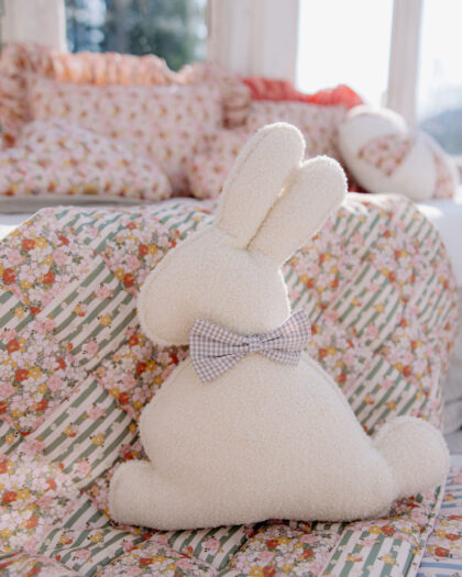 Miękki pluszowy zając z kokardką siedzący na kwiecistym patchworkowym kocu przy oknie