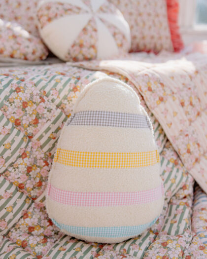 Miękka poduszka w kształcie jajka z kolorowymi pasami na kwiatowym narzucie na łóżku