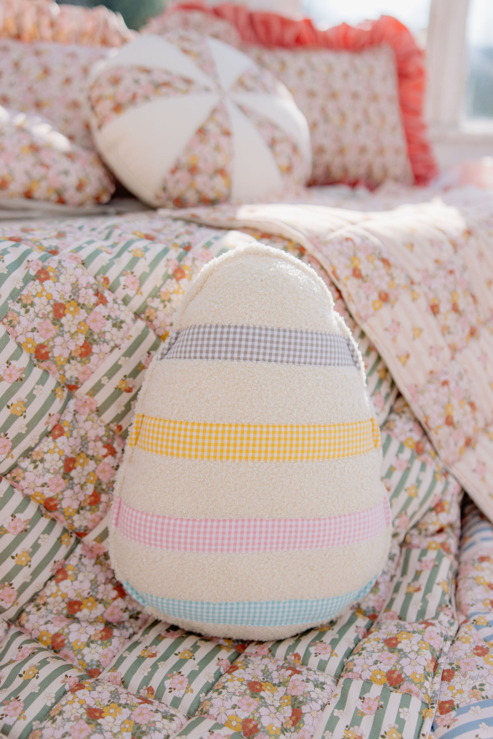 Miękka poduszka w kształcie jajka z kolorowymi pasami na kwiatowym narzucie na łóżku