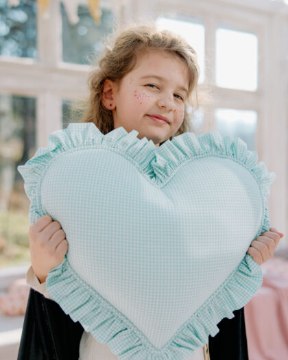 Dziewczynka trzyma dużą miętową poduszkę w kształcie serca w jasnym, słonecznym pomieszczeniu