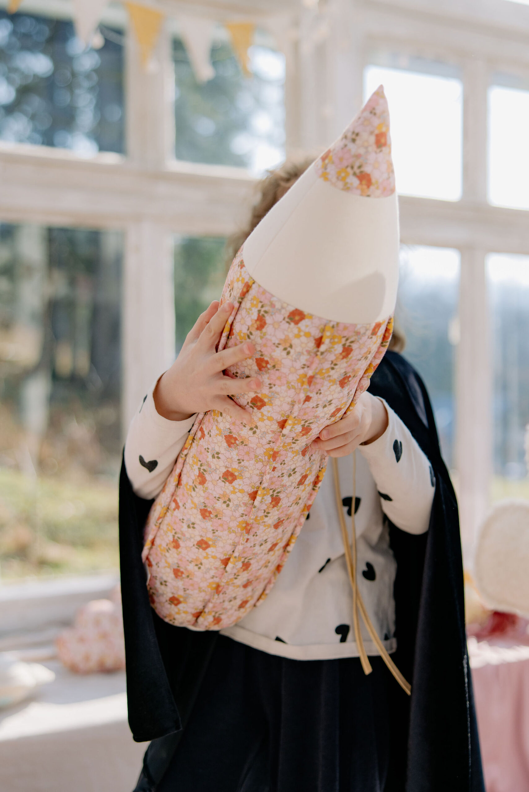 Dziecko trzyma dużą poduszkę w kształcie kolorowej kredki w jasnym, słonecznym pokoju