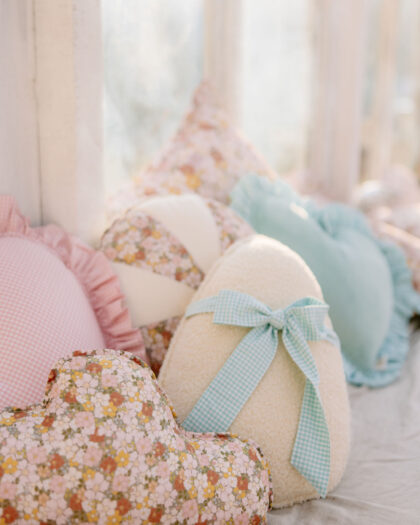 Miękkie poduszki w pastelowych kolorach i wzory kwiatuszków na jasnym tle przy oknie