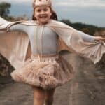 Uśmiechnięta dziewczynka w koronie i tiulowej spódniczce biega po wiejskiej drodze na tle pochmurnego nieba