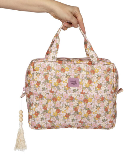 Ręka trzyma kolorową torebkę z kwiatowym wzorem i z frędzlem z drewnianych koralików
