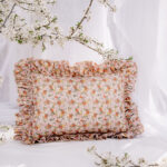 Poduszka ozdobna w drobne kwiaty z falbanami na tle białej tkaniny i kwitnące gałązki